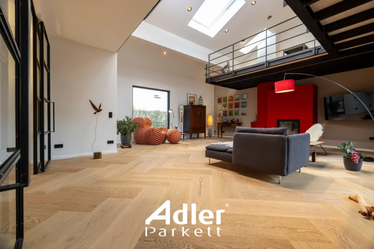 Geräumiges, modernes Wohnzimmer mit hellem Adler Parkett im Fischgrätmuster, hohen Decken und einer Galerie. Roter Kamin und bunte Sitzsäcke.