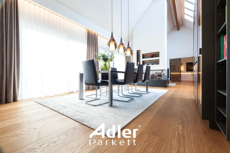 Elegantes Esszimmer mit großem Esstisch, dunklen Stühlen und hellem Adler Parkett. Hohe Fenster und moderne Hängelampen.