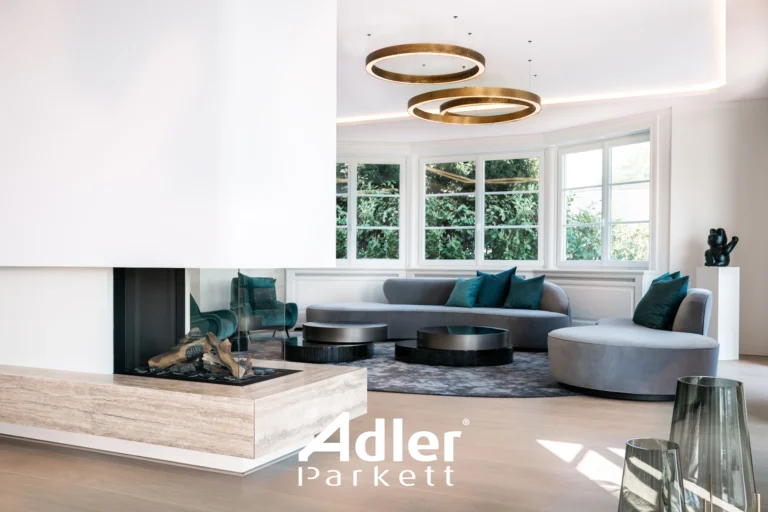 Helles Wohnzimmer mit Adler Parkett, großem Kamin, runden Fenstern, grauen Sofas und goldfarbenen Ringleuchten.