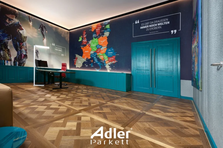 Ein modernes Büro mit einem auffälligen Adler Tafelparkett. Eine Wand ist mit einer bunten Weltkarte und inspirierenden Zitaten dekoriert. Türkise Schränke und Türen ergänzen den Raum.