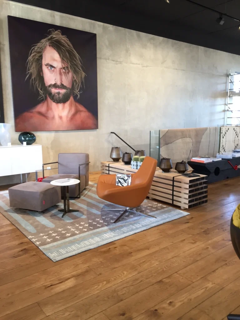 Eine moderne Boutique mit warmem Holzfußboden. Die Wand ziert ein großes Porträt, davor stehen Sessel in Orange und Grau.