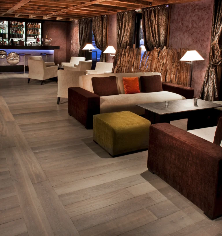 Gemütliche Hotelbar mit heller Holzdecke, Bar, Sofas und rustikalen Vorhängen. Der Bodenbelag ist ein breiter, heller Dielenboden.