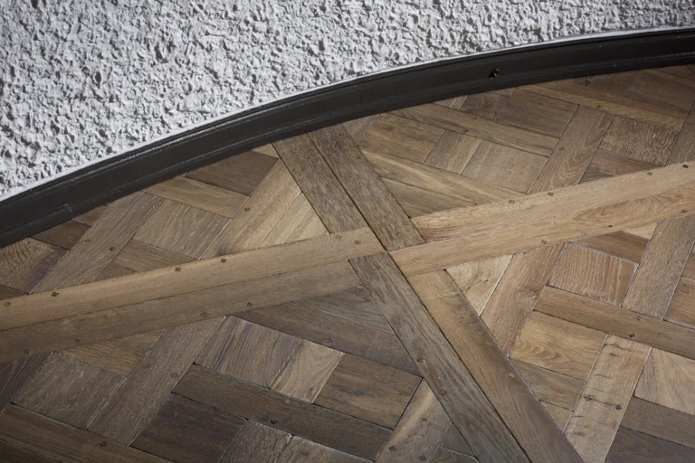 Nahaufnahme eines Parkettbodens im Versailles-Muster aus Holz. Die Holzplanken sind kreisförmig angeordnet und bilden ein traditionelles Muster.